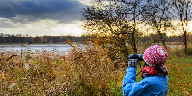 vrouw met winterse kleding en verrekijker in de natuur